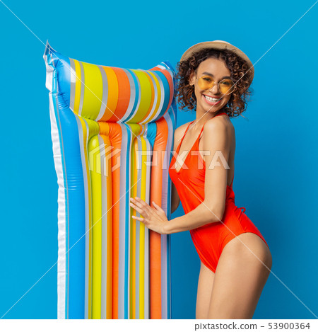 Happy african lady in swimwear smiling with colorful swim mattress Happy african lady in swimwear smiling with colorful swim mattress 53900364