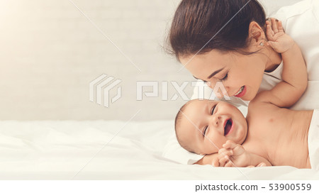 Mother tickling her baby playing in bed at home Mother tickling her baby playing in bed at home 53900559
