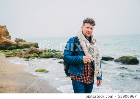 Traveler with a backpack standing near a beautiful sea with waves, a stylish hipster boy posing near Traveler with a backpack standing near a beautiful sea with waves, a stylish hipster boy posing near 53900967