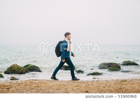 Traveler with a backpack standing near a rock against a beautiful sea with waves, a stylish hipster Traveler with a backpack standing near a rock against a beautiful sea with waves, a stylish hipster 53900968