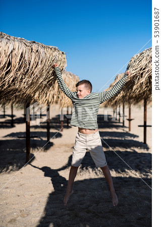A small boy playing outdoors on sand beach, jumping. 53901687
