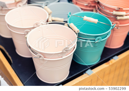 Various multicolored bright small ornamental metal buckets for sale on wooden table outdoors. Many Various multicolored bright small ornamental metal buckets for sale on wooden table outdoors. Many 53902299