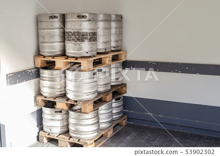 Used metal beer keg barrel on wooden pallets in corner of warehouse after delivery. Steel drink 53902302