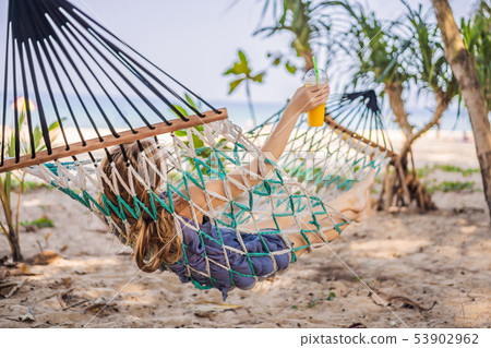 Young woman on the beach in a hammock with a drink 53902962