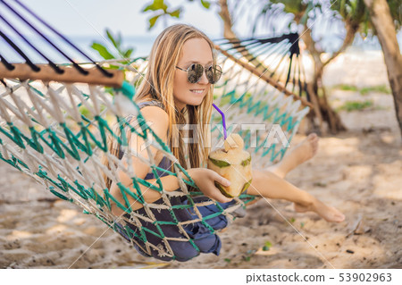 Young woman on the beach in a hammock with a drink 53902963
