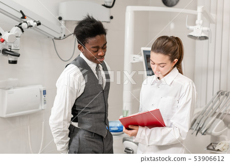 African male patient in dental clinic. Young Woman dentist makes a diagnosis and records 53906612