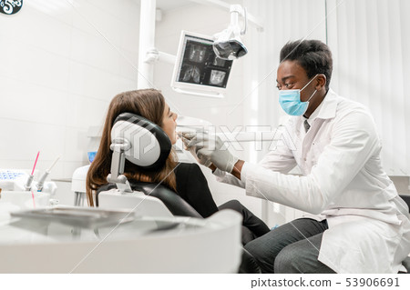 Doctor treats teeth. Young African male dentist with a patient. Woman in the dentist chair at dental 53906691