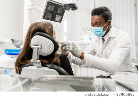Doctor treats teeth. Young African male dentist with a patient. Woman in the dentist chair at dental Doctor treats teeth. Young African male dentist with a patient. Woman in the dentist chair at dental 53906692