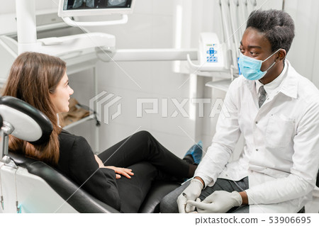 Young African male dentist with a patient. Woman in the dentist chair at dental clinic. Medicine 53906695
