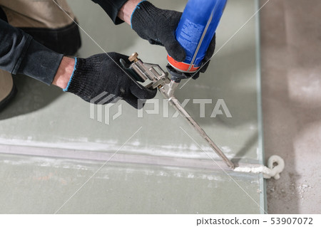 Worker is using a polyurethane foam for gluing drywall at ninety degrees. Hand holding polyurethane Worker is using a polyurethane foam for gluing drywall at ninety degrees. Hand holding polyurethane 53907072