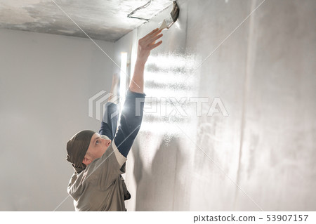 Young repairman smear on wall glue with a brush. Worker glueing wallpapers on concrete wall. Repair Young repairman smear on wall glue with a brush. Worker glueing wallpapers on concrete wall. Repair 53907157