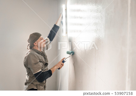 Young repairman smear on wall glue with a roller. . Worker glueing wallpapers on concrete wall Young repairman smear on wall glue with a roller. . Worker glueing wallpapers on concrete wall 53907158