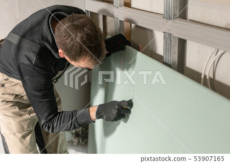 A man working Builder makes a marking on the drywall for electrical wiring. Metal drywall 53907165