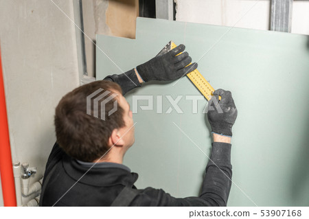 A man working Builder makes a marking on the drywall for electrical wiring. Metal drywall A man working Builder makes a marking on the drywall for electrical wiring. Metal drywall 53907168