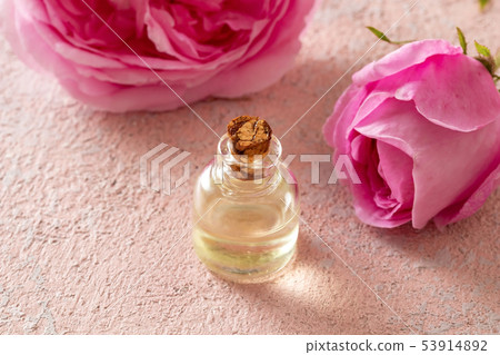 A bottle of rose essential oil with rose flowers 53914892