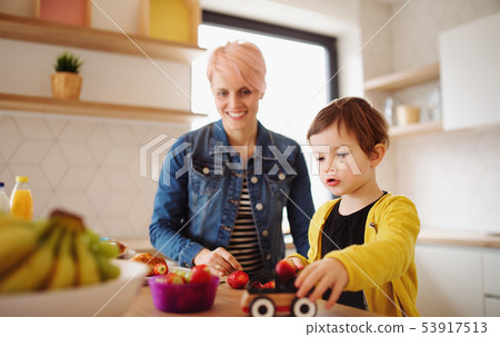 A young mother with small daughter eating fruit in a kitchen. 53917513