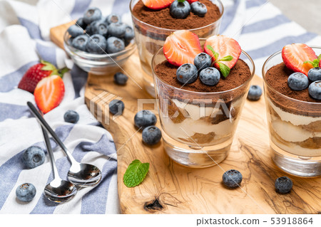 Classic tiramisu dessert with blueberries and strawberries in a glass on concrete background Classic tiramisu dessert with blueberries and strawberries in a glass on concrete background 53918864