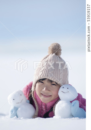 Smiling girl with a snowman in a snowy field 53919157
