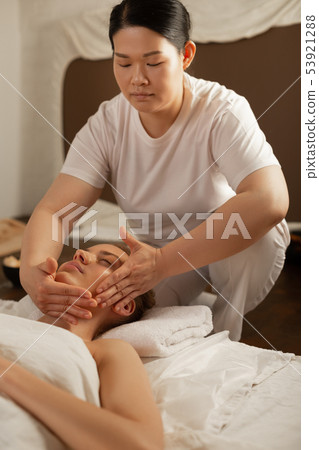 Focused dark-haired Asian master pressing on parts of client face Focused dark-haired Asian master pressing on parts of client face 53921288
