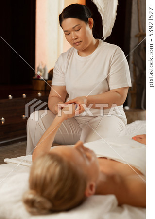 Concentrated professional masseuse in white uniform dealing with palms Concentrated professional masseuse in white uniform dealing with palms 53921527