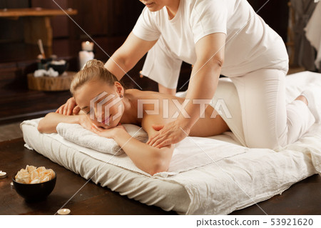 Masseuse in white uniform sitting on the back of her client Masseuse in white uniform sitting on the back of her client 53921620