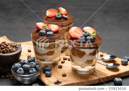 Classic tiramisu dessert with blueberries and strawberries in a glass on dark concrete background 53923016