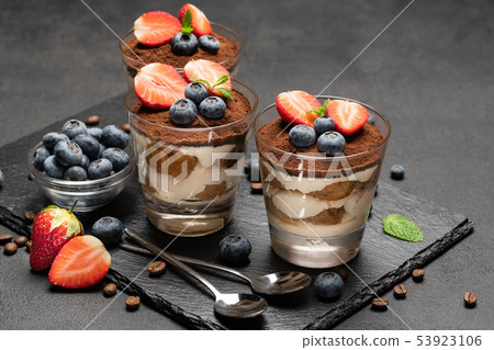 Classic tiramisu dessert with blueberries and strawberries in a glass on dark concrete background 53923106