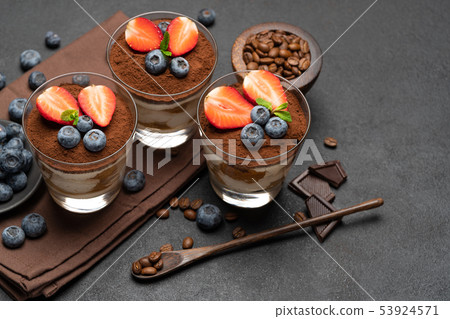 Classic tiramisu dessert with blueberries and strawberries in a glass on dark concrete background 53924571