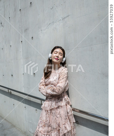 A young female model leaning against a concrete wall in Namsan, Seoul, listening to music with headphones A young female model leaning against a concrete wall in Namsan, Seoul, listening to music with headphones 53927039