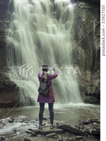 Girl photographs a waterfall with a phone Girl photographs a waterfall with a phone 53927585