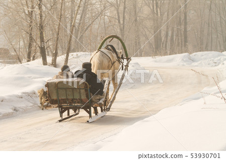 a villager in a village goes in a makeshift sleigh and runs a horse, a clear winter day 53930701