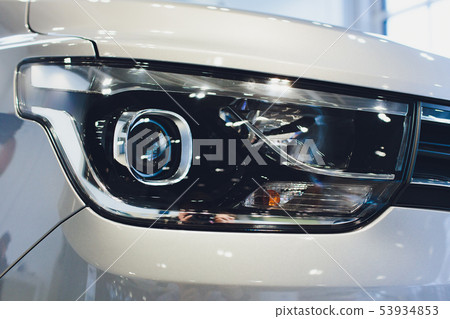Close up of headlight detail of modern luxury car with projector lens for low and high beam. Front Close up of headlight detail of modern luxury car with projector lens for low and high beam. Front 53934853