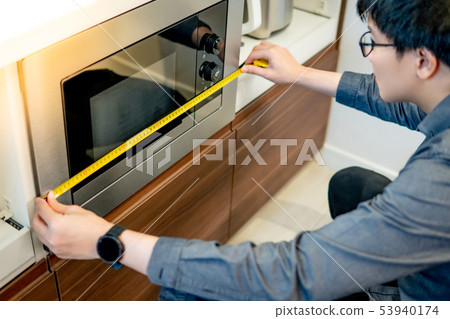 Asian man using tape measure on microwave Asian man using tape measure on microwave 53940174