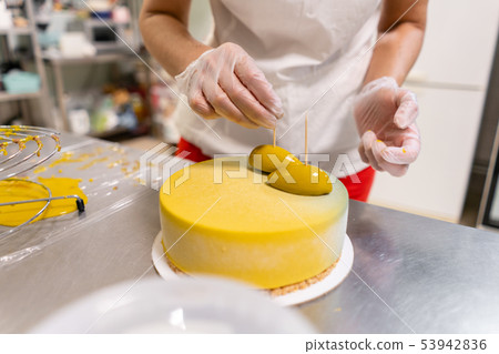 Pastry chef decorates Modern european cake. Mousse dessert covered with yellow velour. Sweet dessert Pastry chef decorates Modern european cake. Mousse dessert covered with yellow velour. Sweet dessert 53942836