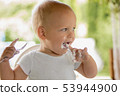 Cute funny little blonde toddler boy eating delicious yogurt sitting outdoor 53944900