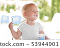 Smiling little blonde toddler boy eating delicious yogurt sitting outdoor 53944901