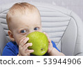 Cute baby 1,4 years old sitting on high children chair and eating green apple alone in white kitchen 53944906