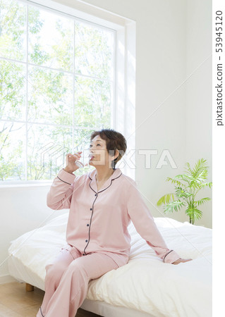 Senior woman in pajamas drinking water on bed 53945120