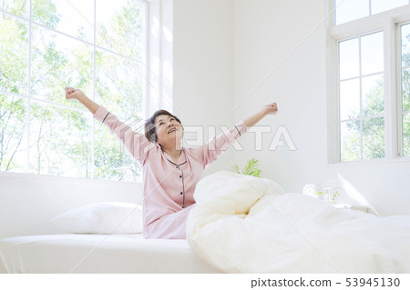 Senior woman in pajamas stretching while sitting in bed 53945130