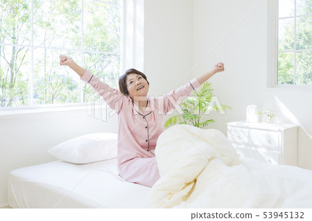 舒展的睡衣的資深婦女,當坐在床上時 舒展的睡衣的資深婦女,當坐在床上時 53945132