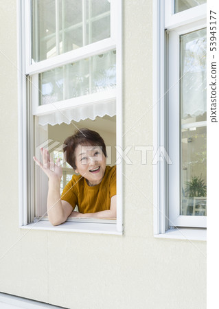 Smiling senior lady waving hand from window Smiling senior lady waving hand from window 53945177