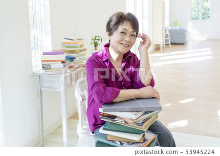 Senior woman touching glasses leaning on stacked books 53945224