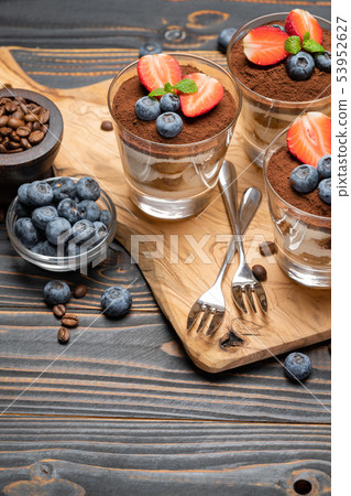 Classic tiramisu dessert with blueberries and strawberries in a glass on wooden background Classic tiramisu dessert with blueberries and strawberries in a glass on wooden background 53952627