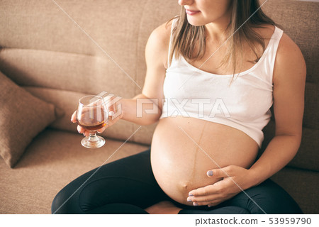 Young future mother keeping glass with alcohol Young future mother keeping glass with alcohol 53959790