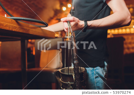Hookah bowl with coal for smoking closeup. Hands holding forceps for shisha hookah and adjusts hot Hookah bowl with coal for smoking closeup. Hands holding forceps for shisha hookah and adjusts hot 53970274
