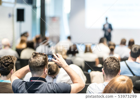 Male business speaker giving a talk at business conference event. Rear view of unrecognized 53973299