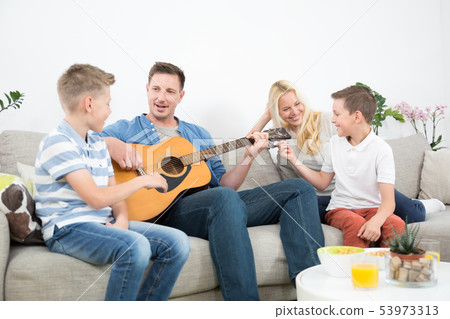 Happy caucasian family smiling, playing guitar and singing songs together at cosy modern home Happy caucasian family smiling, playing guitar and singing songs together at cosy modern home 53973313