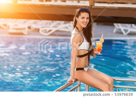 beautiful woman with a cocktail sitting on a handrail of a pool beautiful woman with a cocktail sitting on a handrail of a pool 53976639