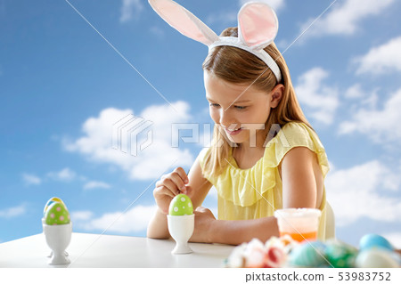 happy girl coloring easter egg over blue sky 53983752