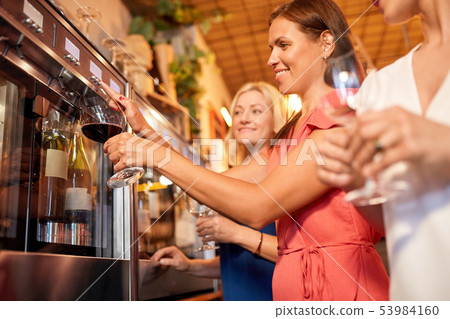 happy women pouring wine from dispenser at bar 53984160